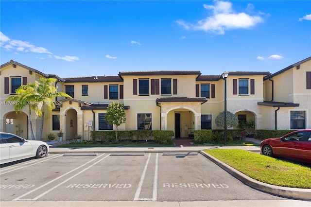 townhome / multi-family property featuring uncovered parking, a tile roof, and stucco siding