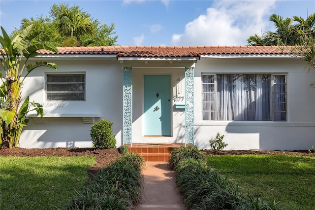 mediterranean / spanish house with stucco siding, a front yard, and a tile roof