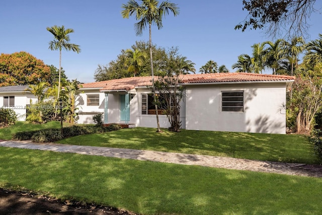 view of front facade with a tiled roof, a front yard, and stucco siding