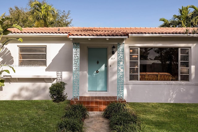 view of exterior entry with a lawn and stucco siding