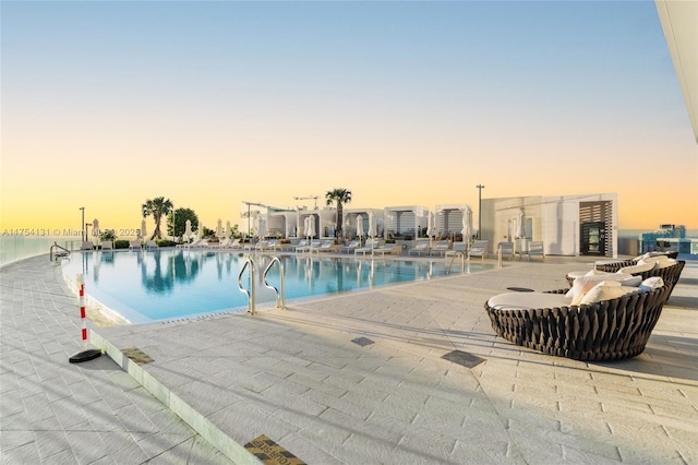 pool at dusk with a community pool and a patio