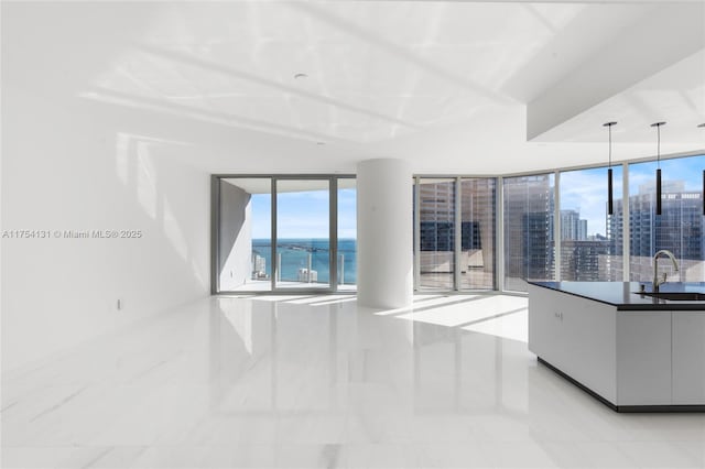 unfurnished living room with a water view, a view of city, a wall of windows, and a sink