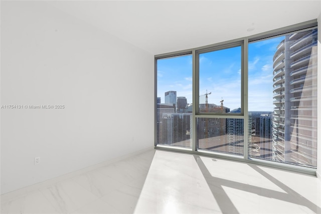 spare room featuring a wall of windows, a view of city, marble finish floor, and baseboards