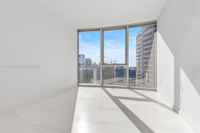 spare room with marble finish floor, baseboards, floor to ceiling windows, and a city view