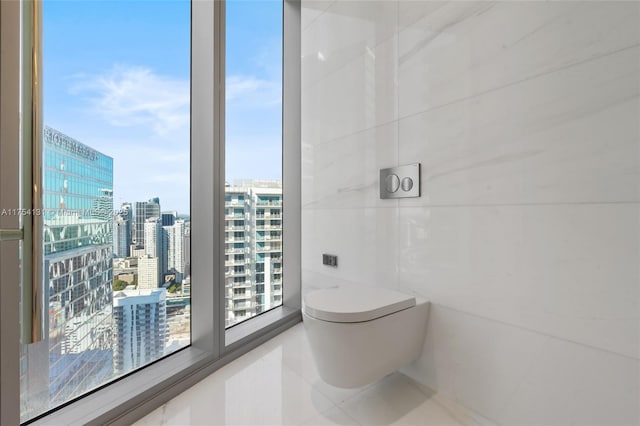 bathroom with a view of city, plenty of natural light, toilet, and tile walls