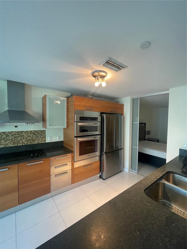 kitchen with light tile patterned floors, visible vents, appliances with stainless steel finishes, wall chimney range hood, and a sink