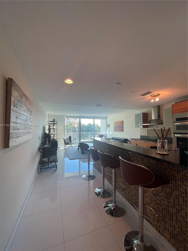 interior space with light tile patterned floors, double oven, visible vents, wall chimney range hood, and dark countertops