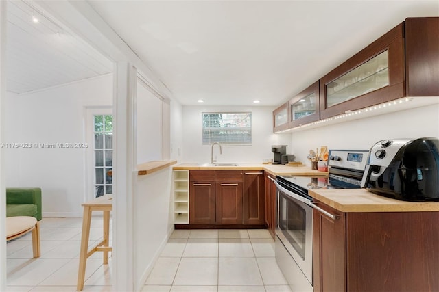 kitchen featuring light tile patterned floors, stainless steel electric range oven, glass insert cabinets, light countertops, and a sink