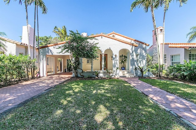 mediterranean / spanish-style home with stucco siding, a tiled roof, decorative driveway, and a front yard