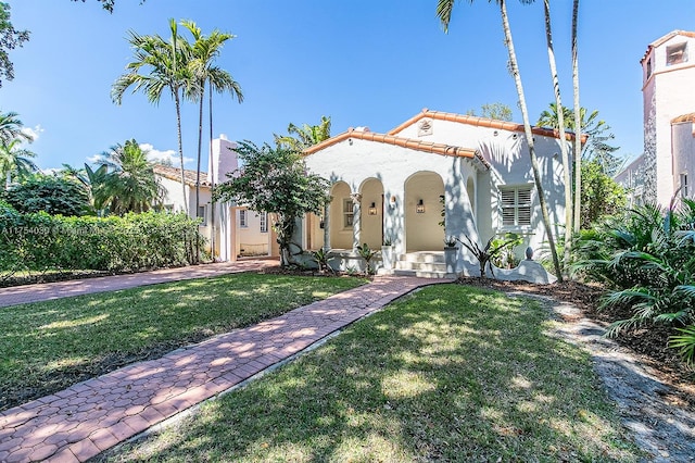 mediterranean / spanish home with a front yard, a tiled roof, and stucco siding