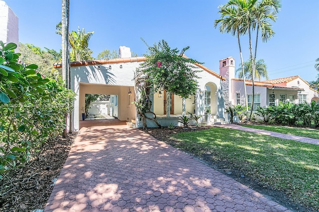 mediterranean / spanish house featuring a chimney, decorative driveway, a front lawn, a carport, and stucco siding