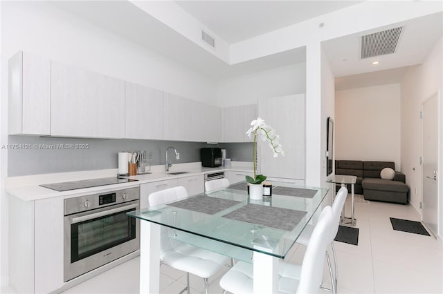 kitchen featuring visible vents, oven, black electric stovetop, light countertops, and a sink