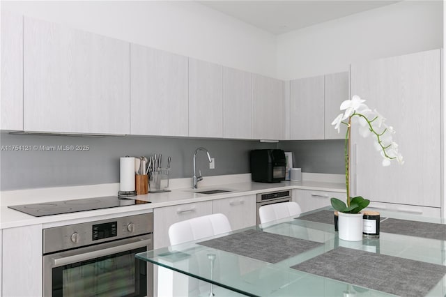 kitchen with light countertops, a sink, modern cabinets, oven, and black electric cooktop