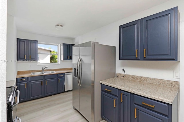 kitchen with light wood-style flooring, blue cabinets, a sink, light countertops, and appliances with stainless steel finishes