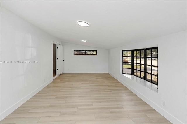 empty room featuring lofted ceiling, light wood-style floors, and baseboards