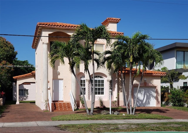 mediterranean / spanish-style house with a garage, a tiled roof, and stucco siding