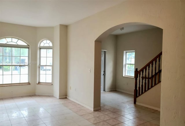 unfurnished room with arched walkways, light tile patterned flooring, stairs, and baseboards