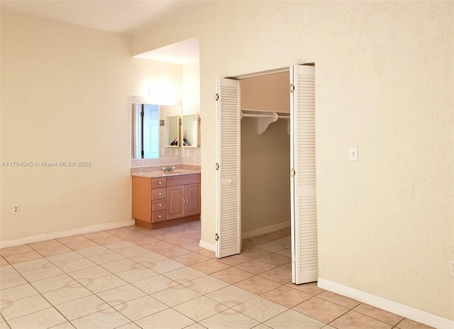 unfurnished bedroom with baseboards, a closet, a sink, and light tile patterned floors