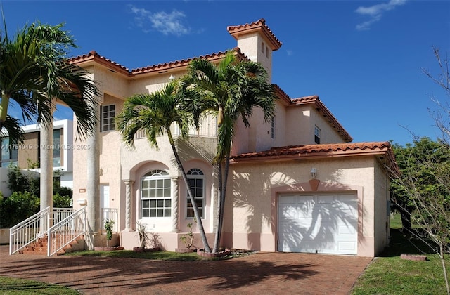 mediterranean / spanish-style house with a garage, a tiled roof, decorative driveway, and stucco siding