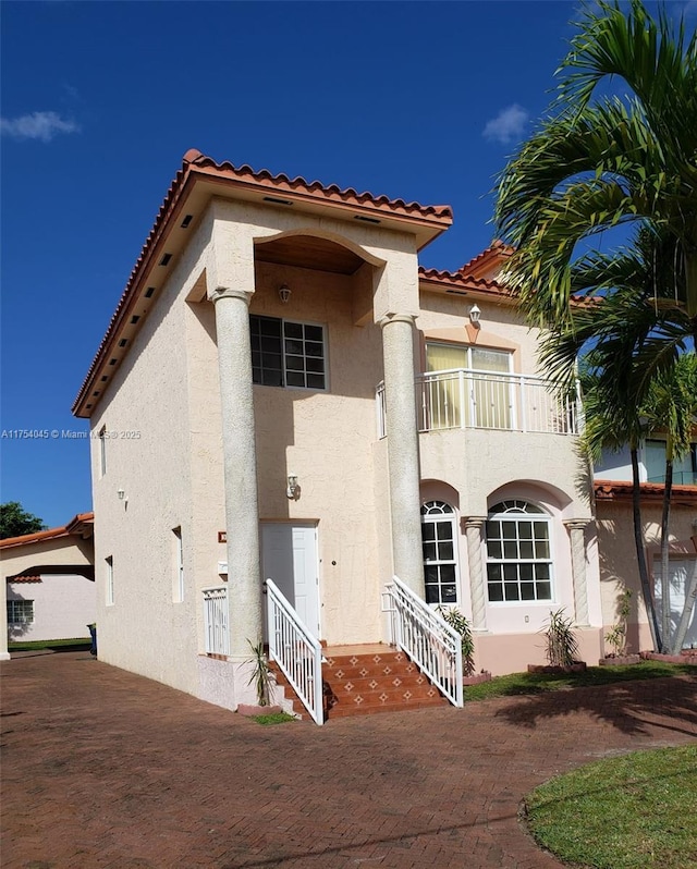view of front of home featuring a tile roof, a balcony, and stucco siding