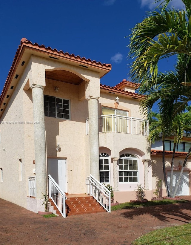 rear view of house featuring entry steps, a tiled roof, a balcony, and stucco siding