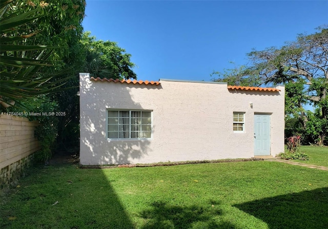 view of side of property with a yard, a tiled roof, and stucco siding