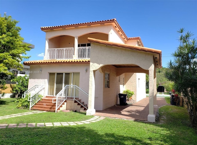 rear view of property with a tile roof, a balcony, a yard, and stucco siding