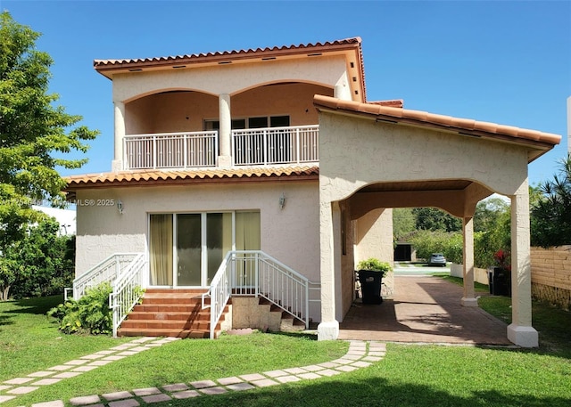 rear view of property with a tiled roof, a balcony, a yard, stucco siding, and a patio