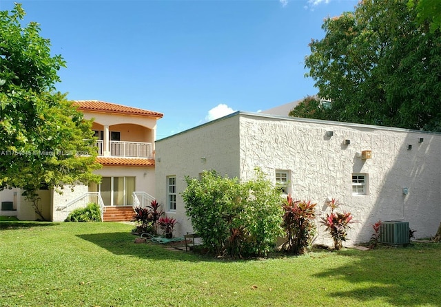 rear view of house with a tile roof, a lawn, a balcony, and stucco siding