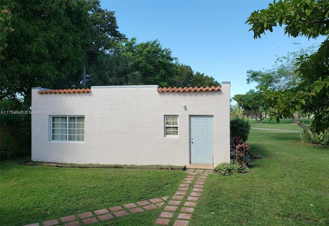 back of property featuring stucco siding, a yard, and a tiled roof