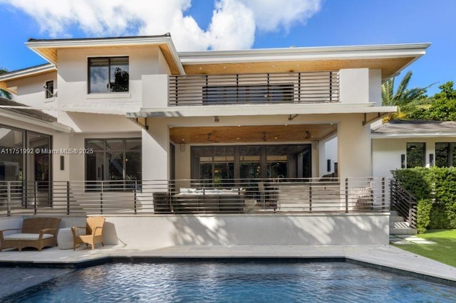 back of property featuring an outdoor pool, a balcony, and stucco siding