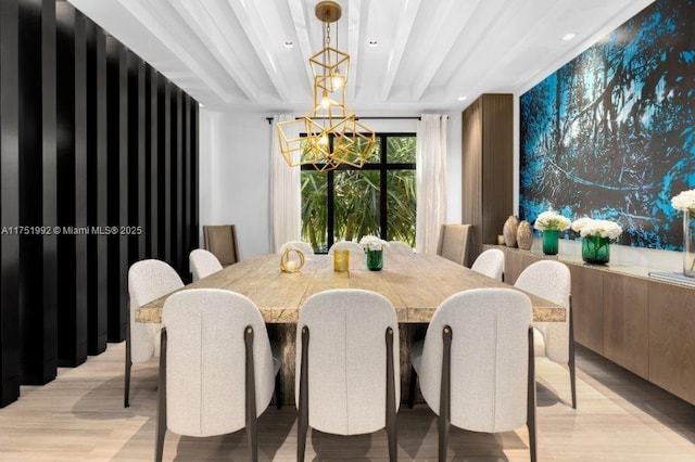 dining area featuring light wood finished floors, an accent wall, a chandelier, and beam ceiling