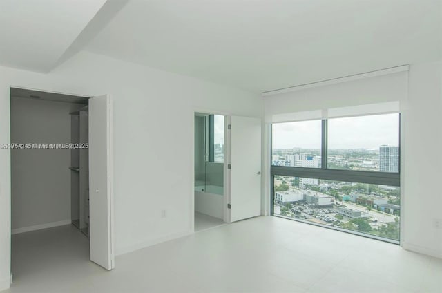 unfurnished bedroom featuring baseboards, a city view, a spacious closet, and ensuite bath