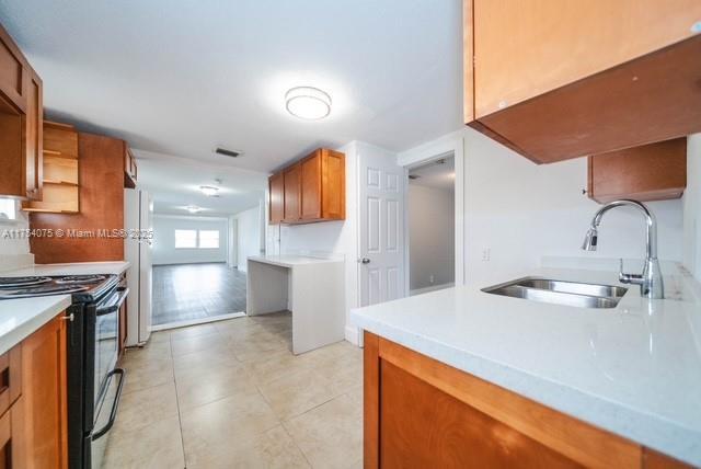 kitchen featuring a sink, black electric range, light countertops, freestanding refrigerator, and brown cabinets