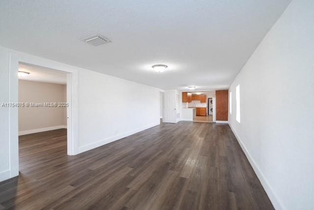 unfurnished living room with baseboards, visible vents, and dark wood-style flooring