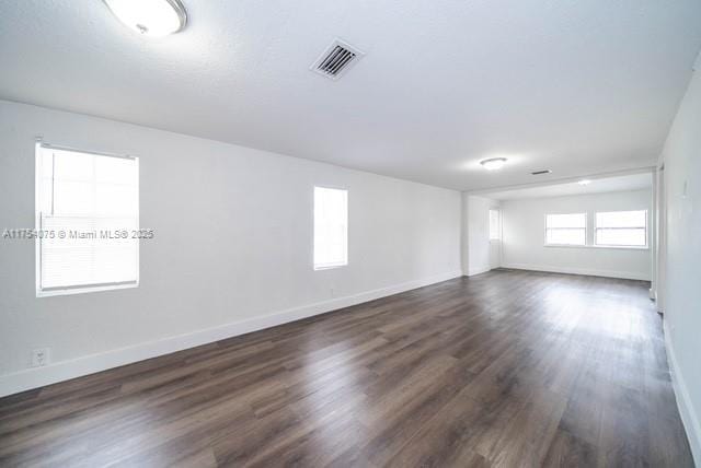 spare room featuring dark wood finished floors, visible vents, and baseboards