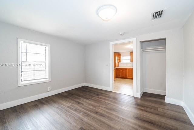 unfurnished bedroom featuring baseboards, a closet, visible vents, and dark wood-style flooring