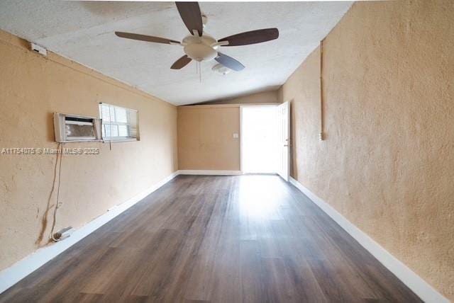 empty room featuring lofted ceiling, dark wood-style flooring, a wall mounted AC, and baseboards