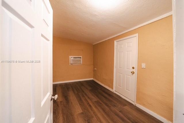 unfurnished room featuring a textured ceiling, baseboards, vaulted ceiling, a wall mounted AC, and dark wood finished floors