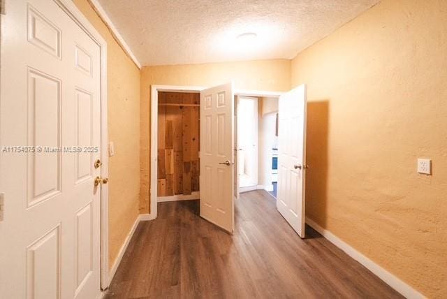 corridor with dark wood-style floors, a textured ceiling, and baseboards