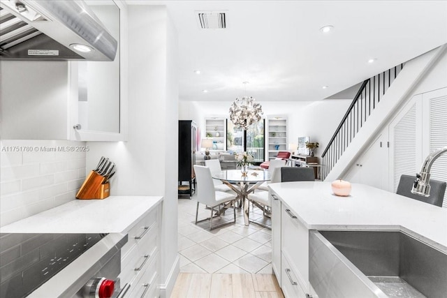 kitchen with tasteful backsplash, visible vents, white cabinets, a sink, and exhaust hood