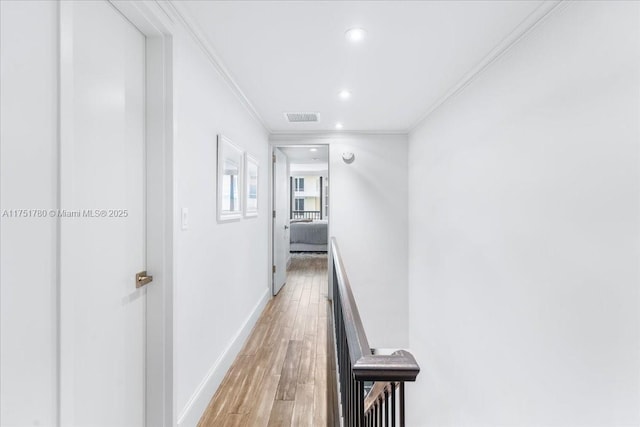 corridor with ornamental molding, light wood-style flooring, visible vents, and baseboards