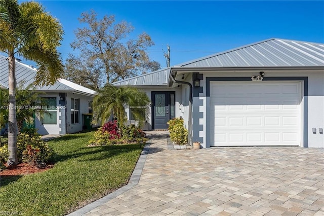 ranch-style house with metal roof, an attached garage, a standing seam roof, a front lawn, and stucco siding