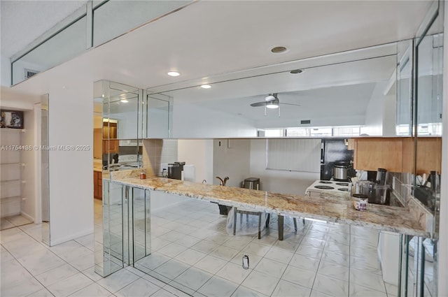 kitchen with a breakfast bar area, a ceiling fan, and light stone countertops