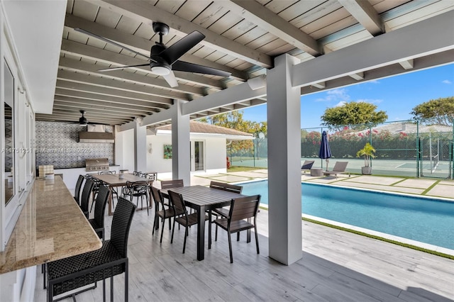 outdoor pool featuring an outdoor kitchen, ceiling fan, grilling area, fence, and outdoor dining space