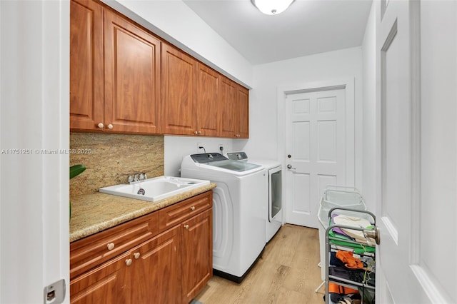 laundry room with washer and clothes dryer, a sink, cabinet space, and light wood-style floors