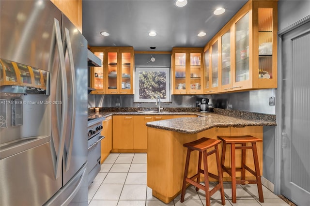 kitchen with a sink, under cabinet range hood, gas range oven, a peninsula, and stainless steel fridge with ice dispenser