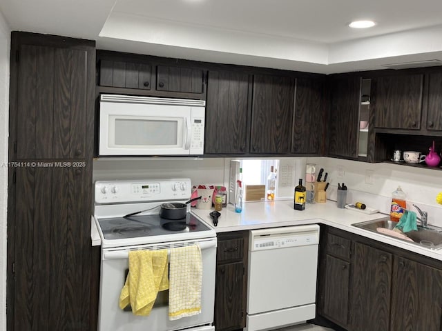 kitchen featuring dark brown cabinetry, white appliances, light countertops, and a sink