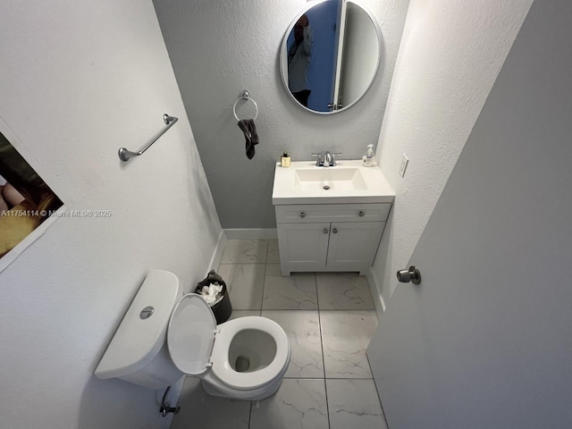 half bath with toilet, marble finish floor, baseboards, and vanity