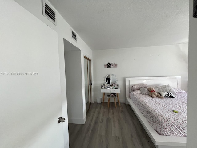 bedroom with a textured ceiling, wood finished floors, visible vents, and baseboards